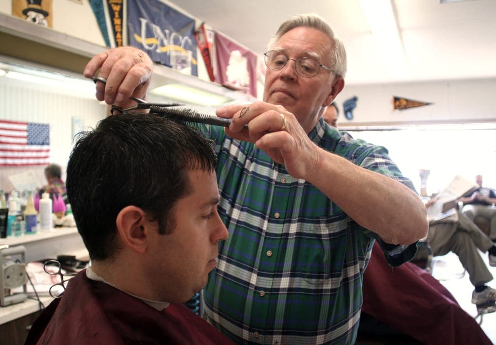 Vieux barbier en chemise à carreaux, peigne et ciseaux au-dessus de la tête d'un client
